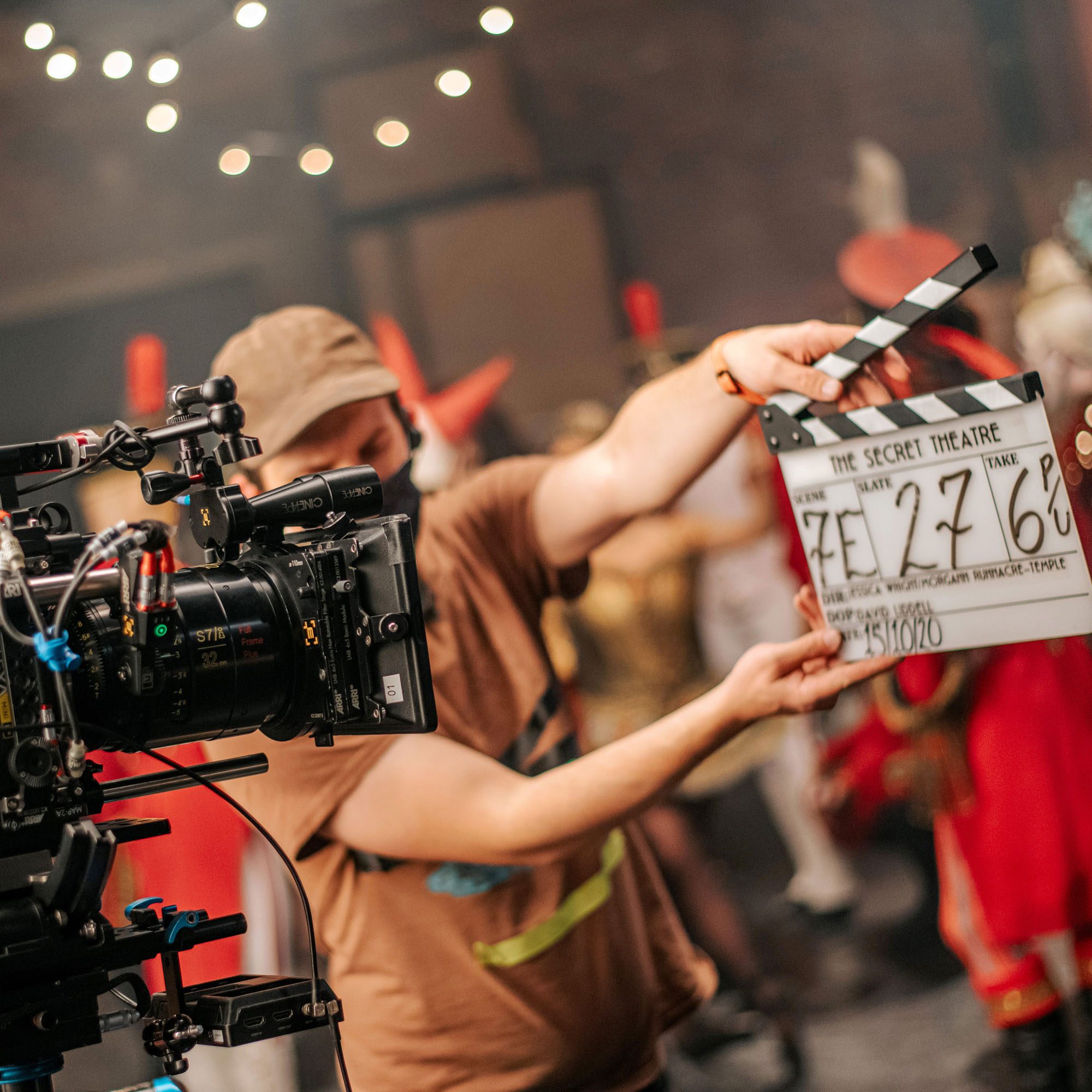 a man behind a camera, holding a clapper board in front of a group of people.