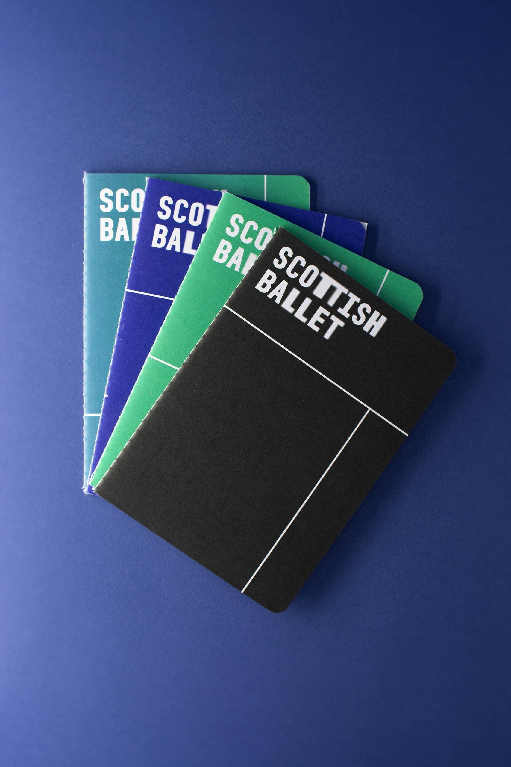 4 A5 notepads with Scottish Ballet logo in white laid out in fan shape