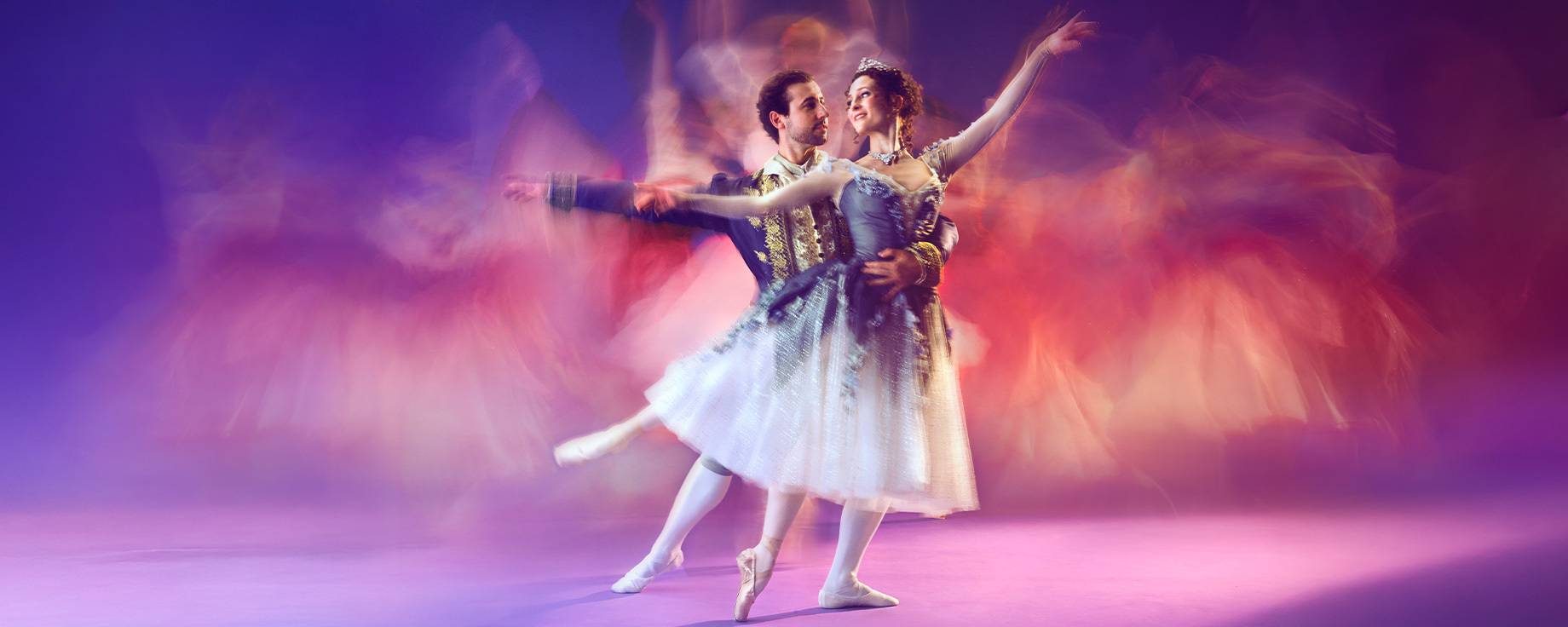 Two ballet dancers in elegant costumes perform a graceful pose on stage, surrounded by colorful motion blur suggesting movement and energy, set against a vibrant purple background.
