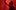 A person with expressive eyes looks upwards whilst bathed in dramatic red light, one hand pressing against a red fabric or screen above them, creating a sense of tension or urgency.